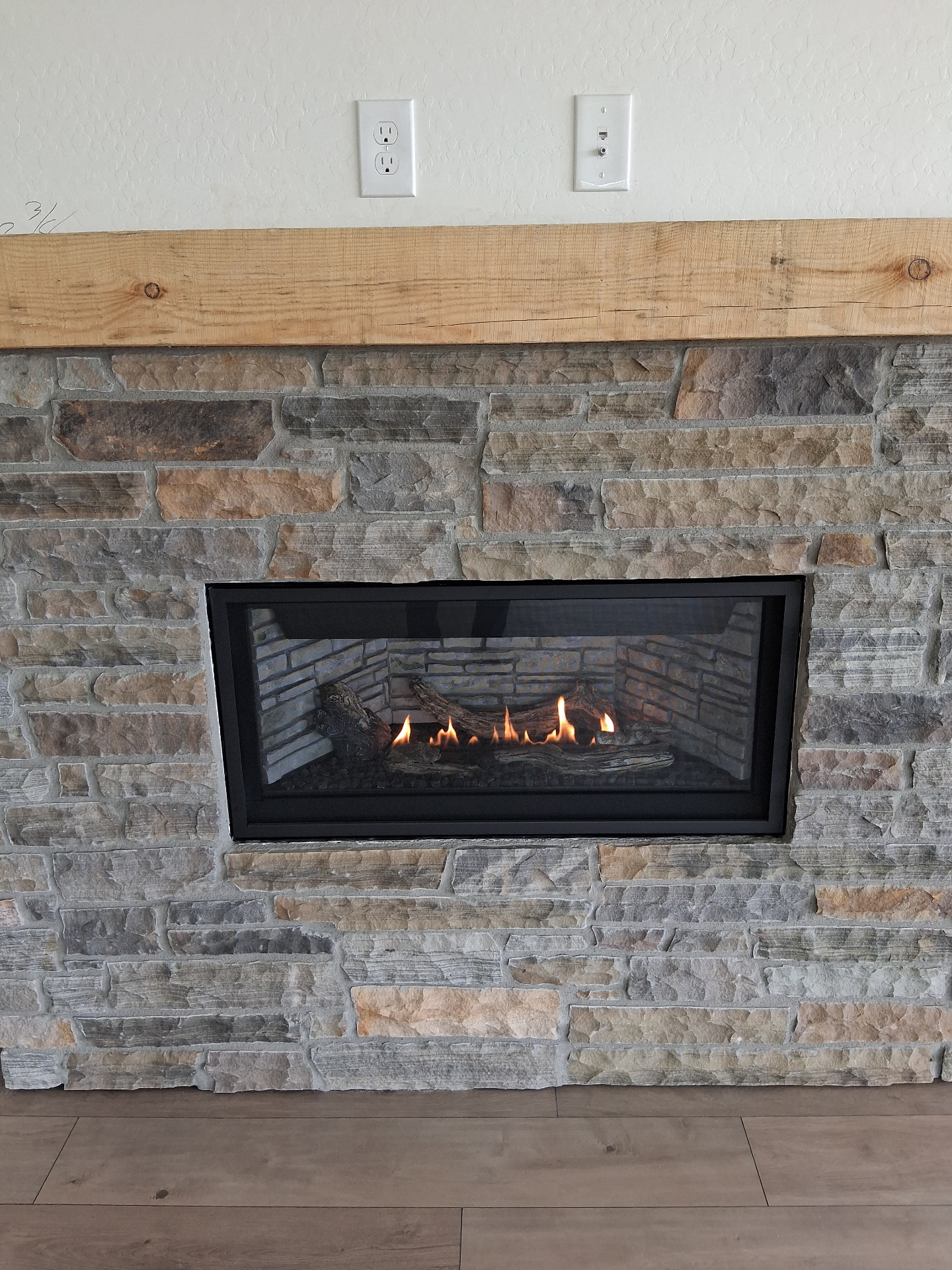 Napoleon Ascent Linear gas fireplace installed in stone wall with wood mantel in Prescott AZ